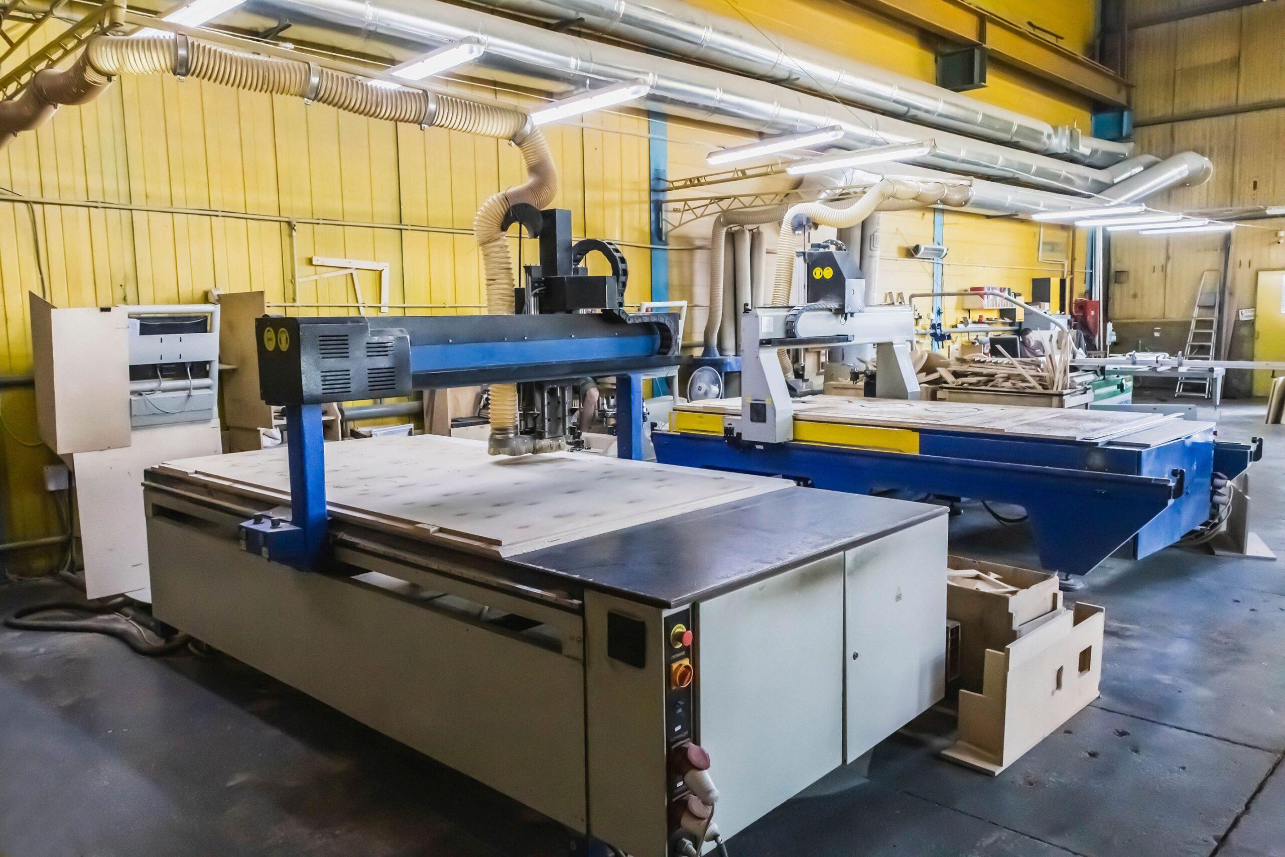 Zwei große CNC-Maschinen schneiden Zuschnitte verschiedener Formen auf einer Sperrholzplatte