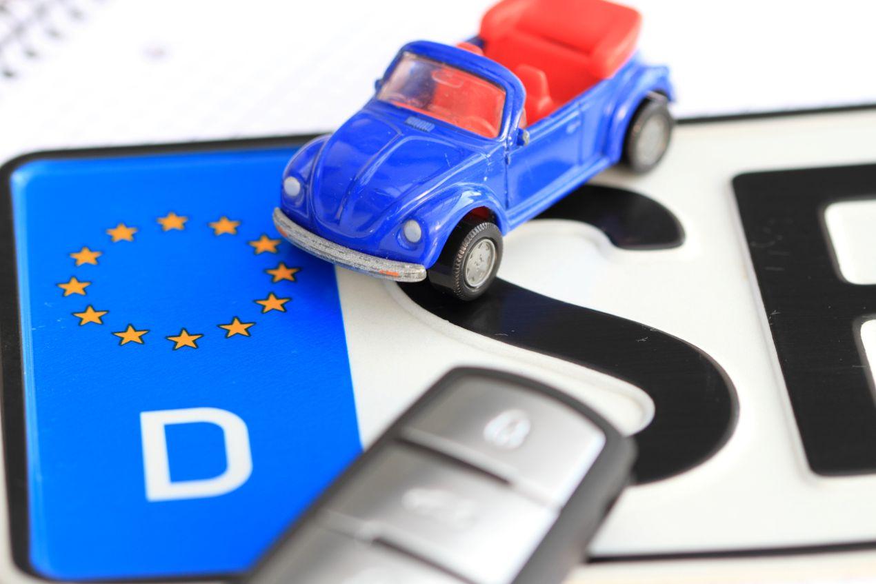 Auto abmelden in München – Symbolbild mit deutschem Kennzeichen, Autoschlüssel und Spielzeugauto auf Nummernschild