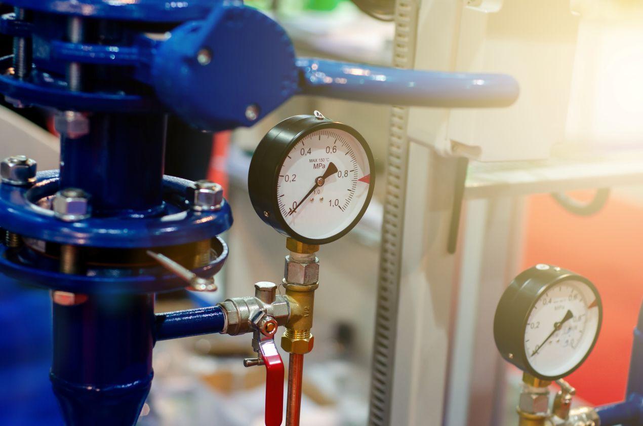 Nahaufnahme eines Manometers zur Druckmessung an einer Hauswasserwerkpumpe mit blauen Metallleitungen und Absperrventil