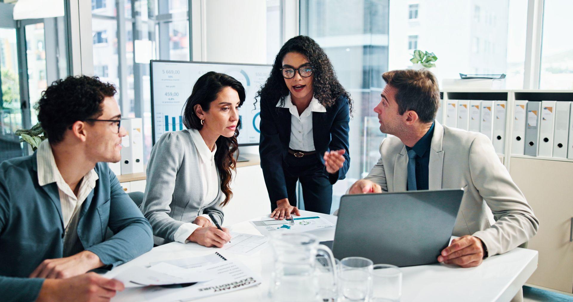 Vier Geschäftsleute diskutieren an einem Konferenztisch mit Diagrammen und Laptop; symbolisiert Analyse, Strategie und Entscheidungsprozesse in der IT Security Beratung.